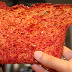 A slice of beetroot bread with orange zest being held up towards the camera