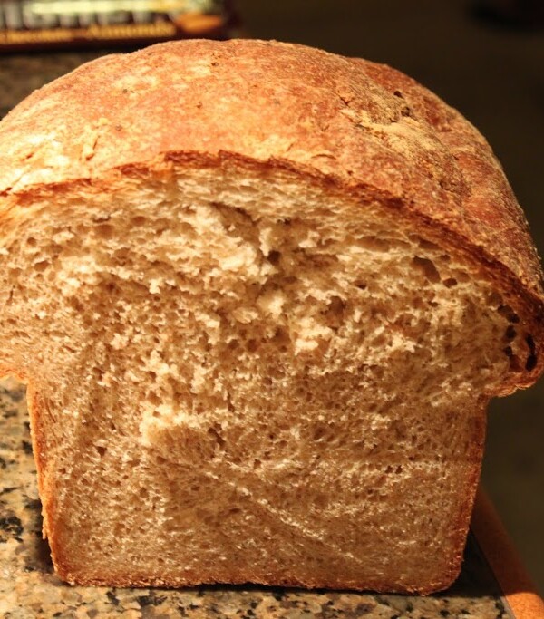 A loaf of wheat oat flax bread cut in half on a work surface