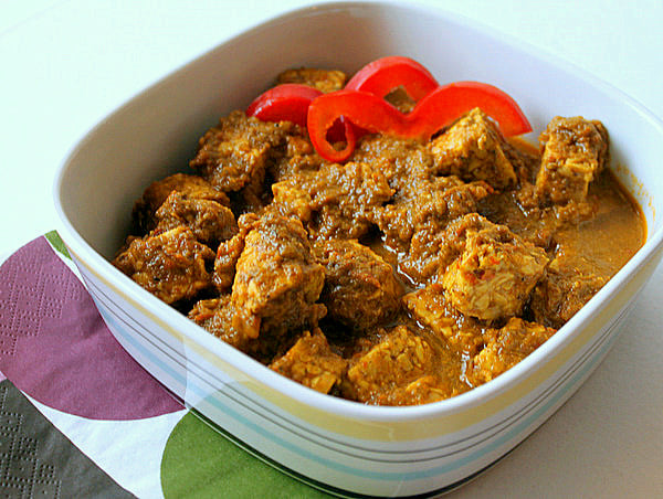 A spinach tomato curry in a white bowl with red pepper garnish