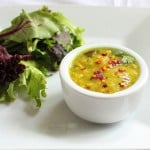 A small white bowl of yellow lentil soup served with salad
