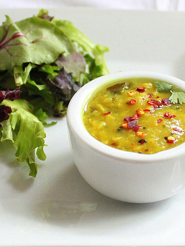 A small white bowl of yellow lentil soup served with salad
