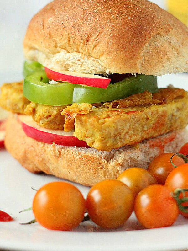 A tempeh frutter in a burger bun served with cherry tomatoes