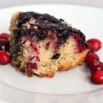 A cranberry and blueberry upside down cake served on a white plate with fresh cramberries