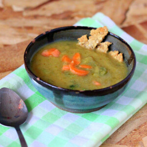 A bowl of Carrot Celery Leek Potato Soup on top of a checked green cloth