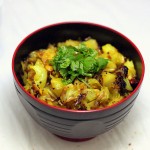 A dark bowl of patta gobi sabzi on a marble countertop