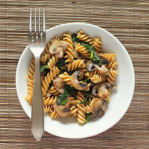 Mushroom fusilli in a white bowl with a fork. On a bamboo mat