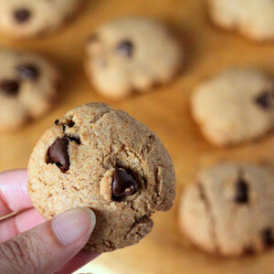Chocolate chip cookies on a work surface with one being held up towards camera