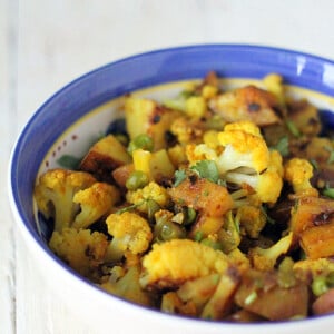 Vegan aloo gobi in a blue rimmed bowl on a white marble worktop