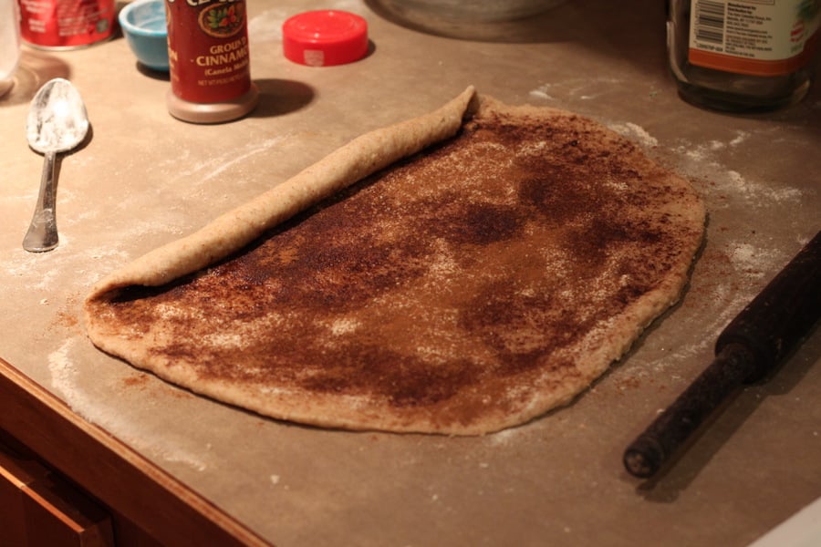 vegan cinnamon rolls rolled out and filled cinnamon roll dough being rolled up to shape buns