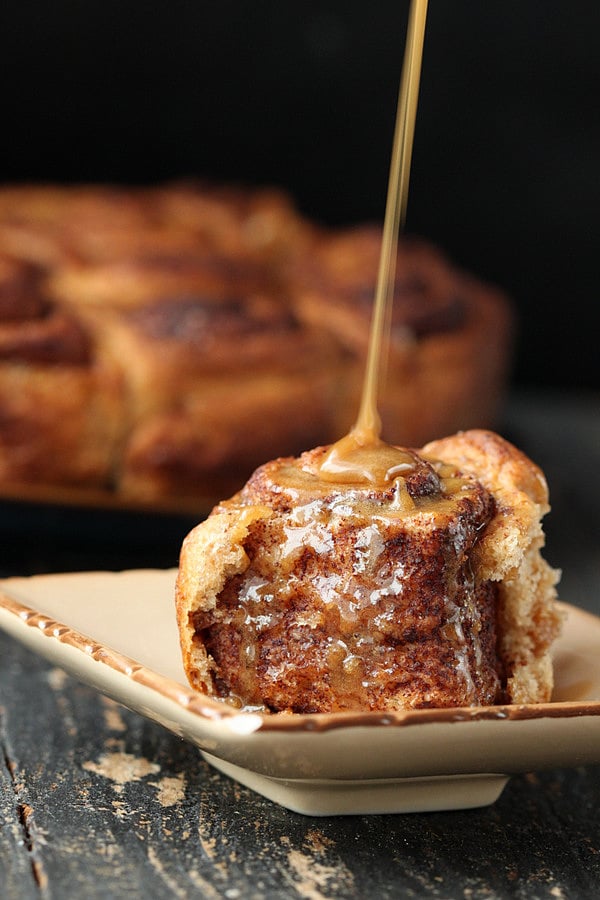 vegan cinnamon rolls side view of a homemade fluffy and soft vegan cinnamon roll being drizzled with maple icing
