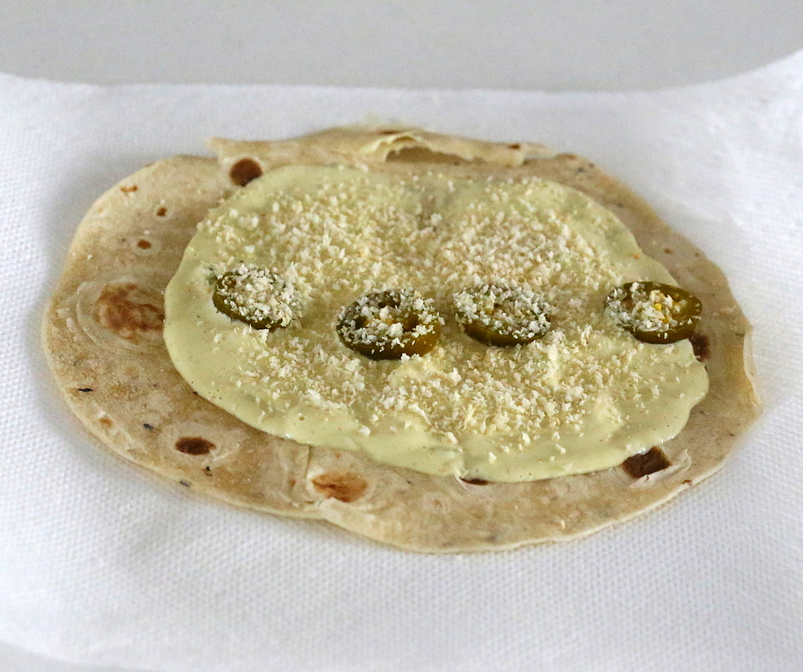 cashew jalapeno popper dip being spread on a wheat tortilla to make vegan breakfast wrap 