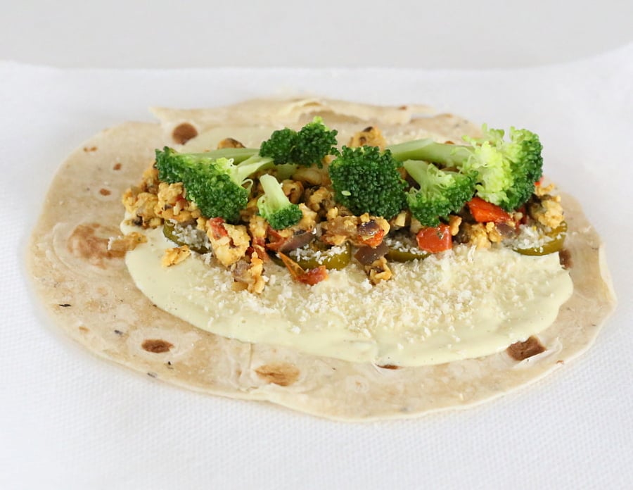 a wrap topped with cashew cream, tempeh scramble and veggies ready to be rolled 