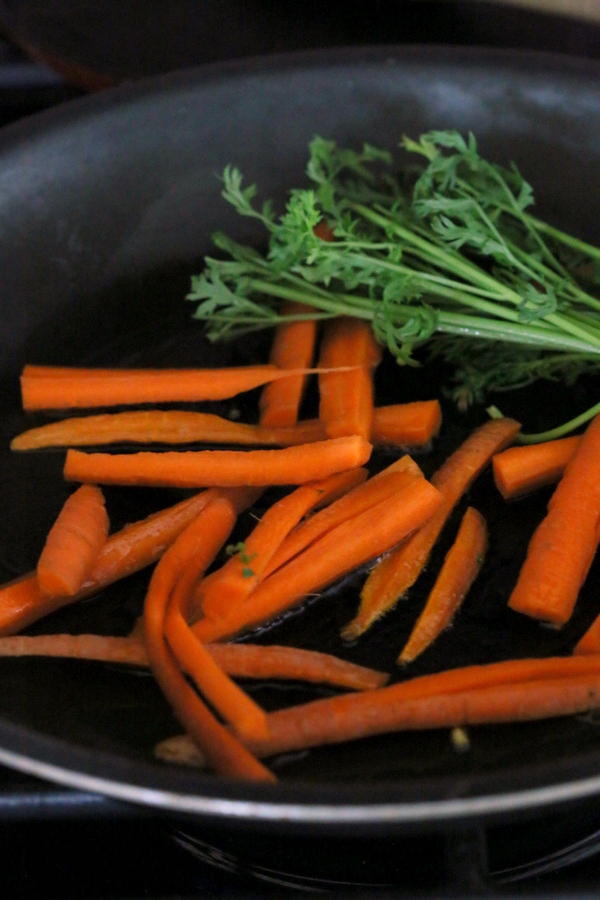 kale salad recipe carrot sticks and carrot greens sauteeing in a black pan