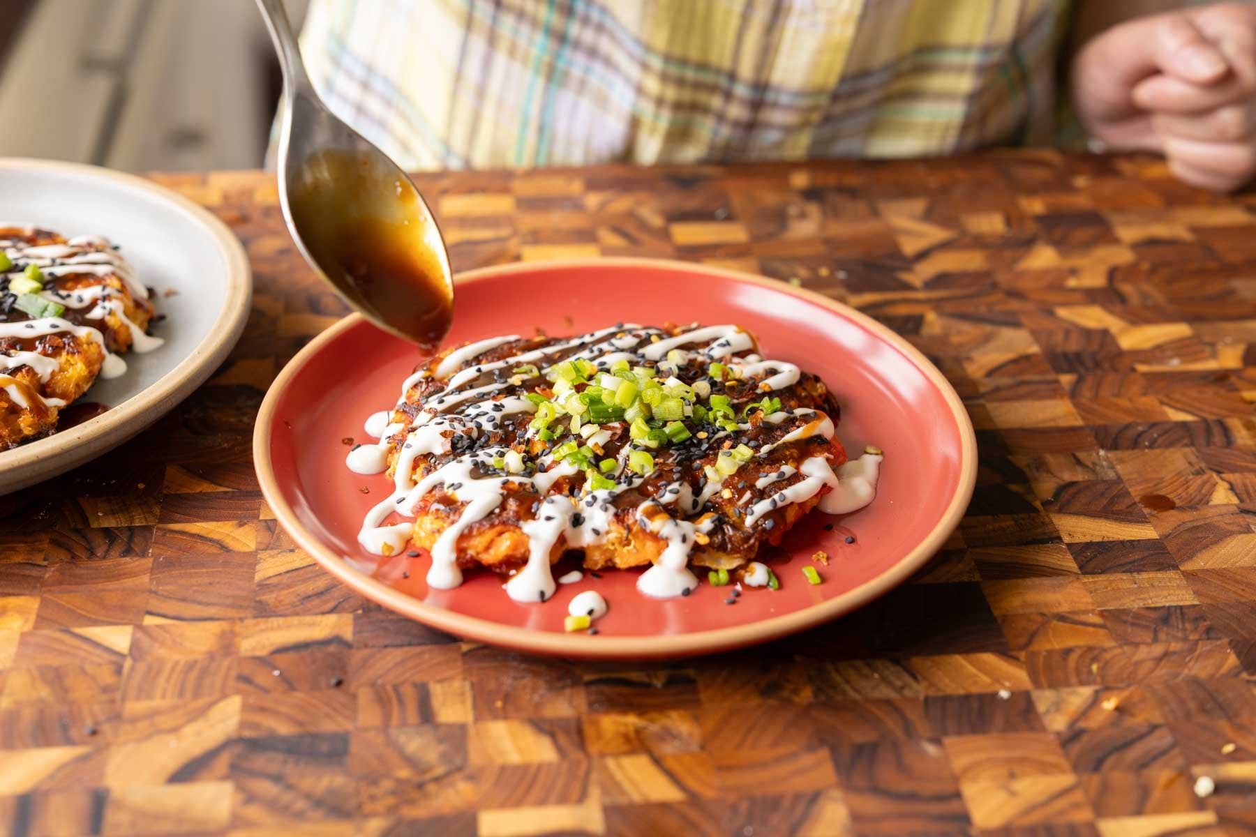 spooning the tonkatsu sauce onto the okonomiyaki
