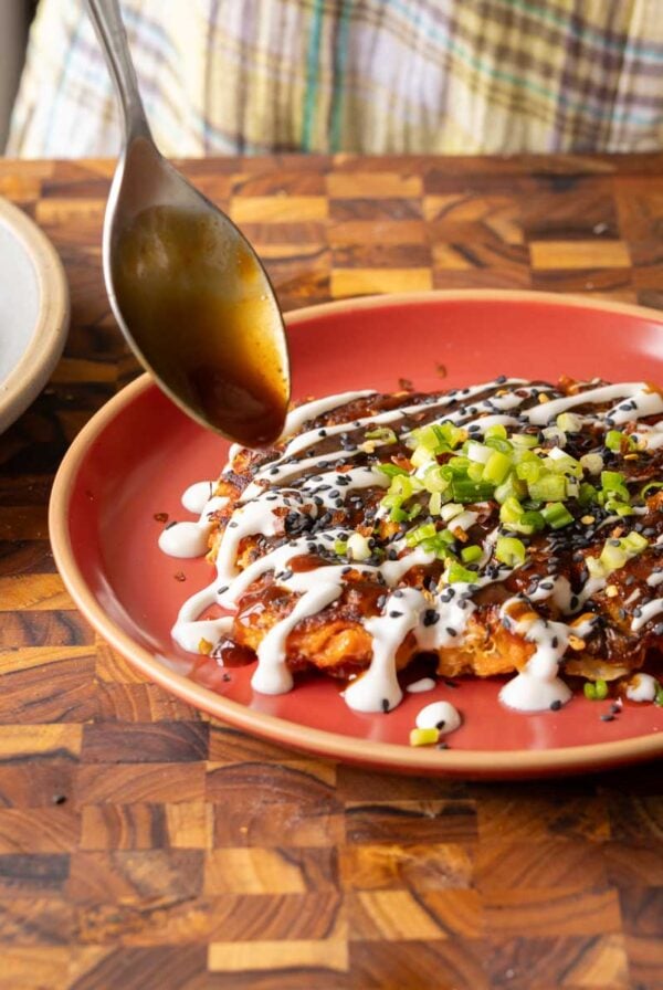 spooning the tonkatsu sauce onto the okonomiyaki