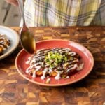 spooning the tonkatsu sauce onto the okonomiyaki