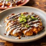 okonomiyaki on a blue plate with green onion and sauces on top