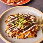 okonomiyaki on a blue plate with green onion and sauces on top