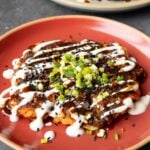 okonomiyaki on a red plate with green onion and sauces on top