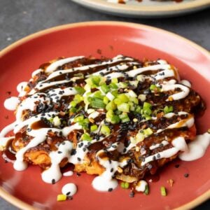 okonomiyaki on a red plate with green onion and sauces on top
