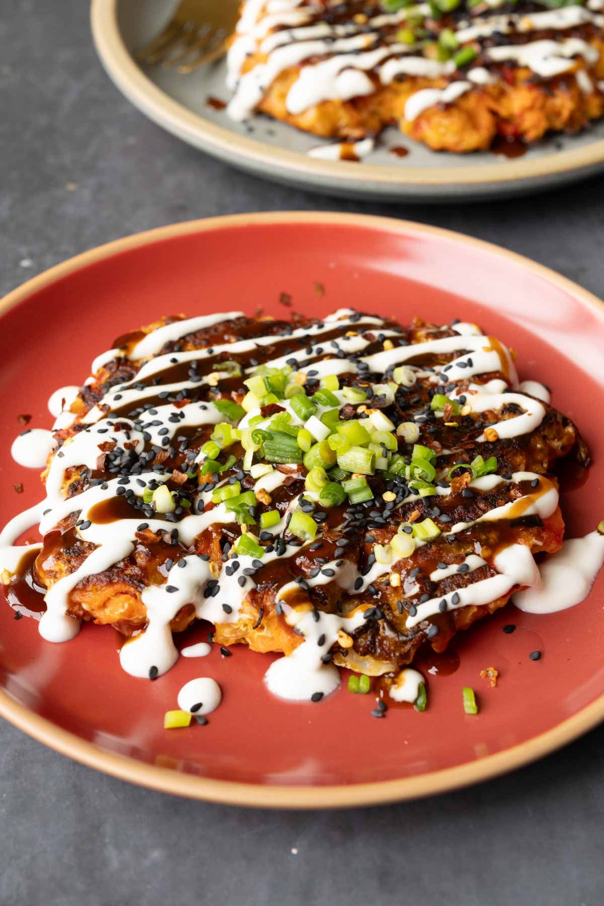 okonomiyaki on a red plate with green onion and sauces on top