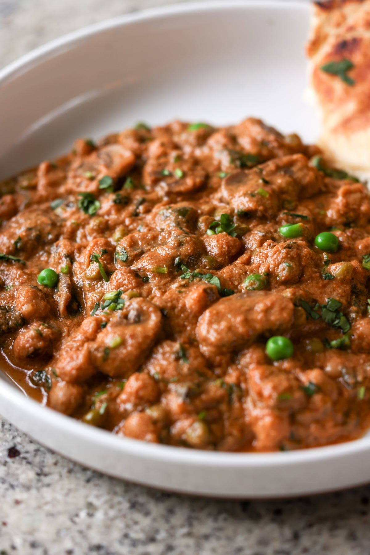 close-up of a bowl of mushroom matar masala with flatbread