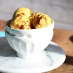 Scoops of vegan mango ice cream in a white bowl on a wooden worktop