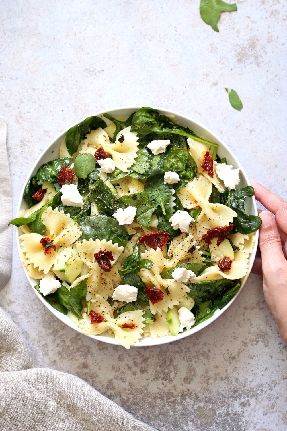 Tuscan Pasta Salad with sun dried tomato, cucumber, spinach, vegan feta in a White Bowl over Concrete