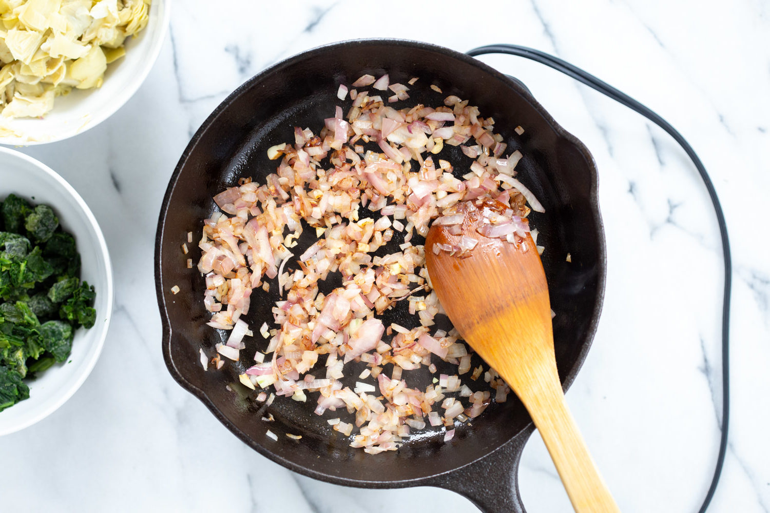 Onion and garlic getting sauteed in a cast iron skillet for our Vegan Spinach Artichoke Dip