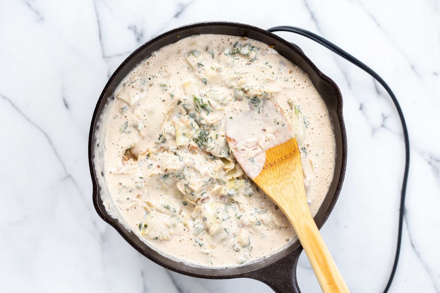 Vegan Spinach Artichoke Dip Process picture with cream sauce added to the spinach artichoke mixture in a cast iron skillet