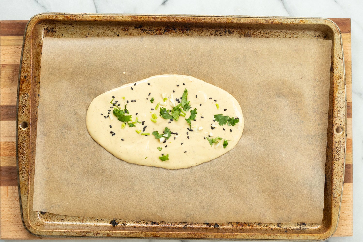 Batter for our Vegan Gluten Free Naan spread on parchment lined baking sheet
