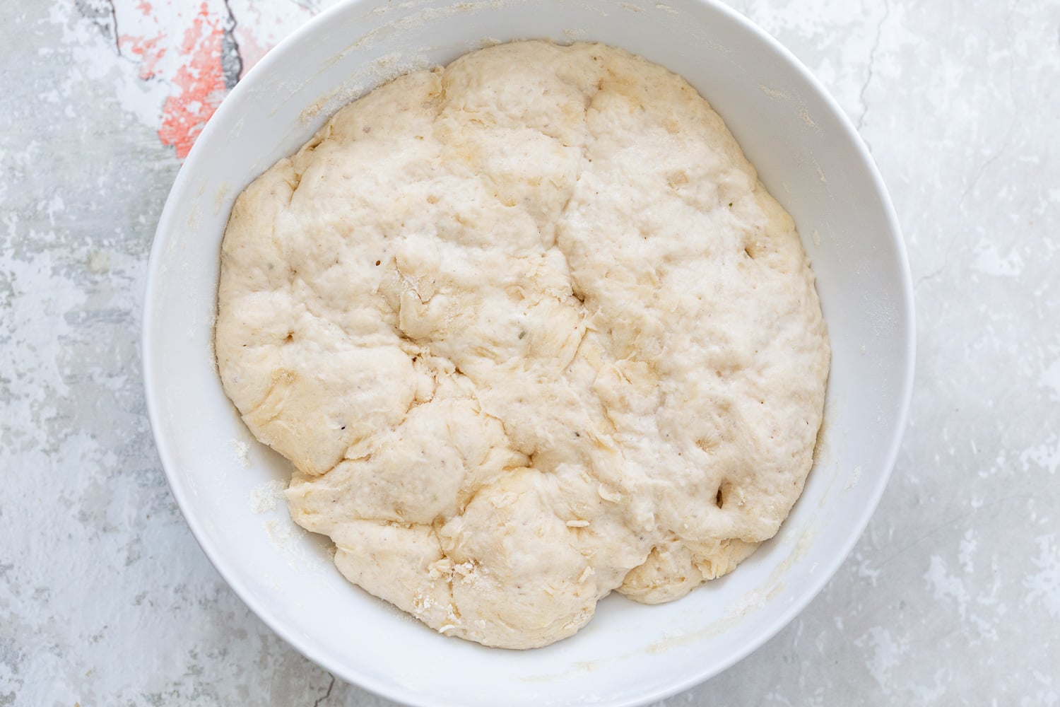 pizza rolls recipe proofed pizza dough doubled in size sitting in a white bowl ready to be punched down