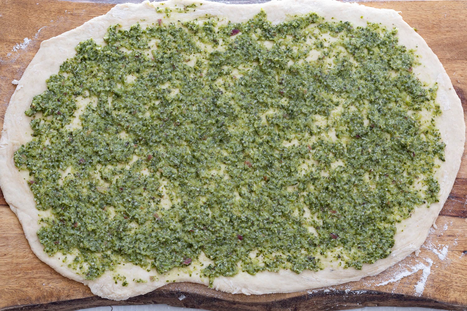 pizza rolls recipe vegan pesto being spread onto rolled out pizza rolls dough