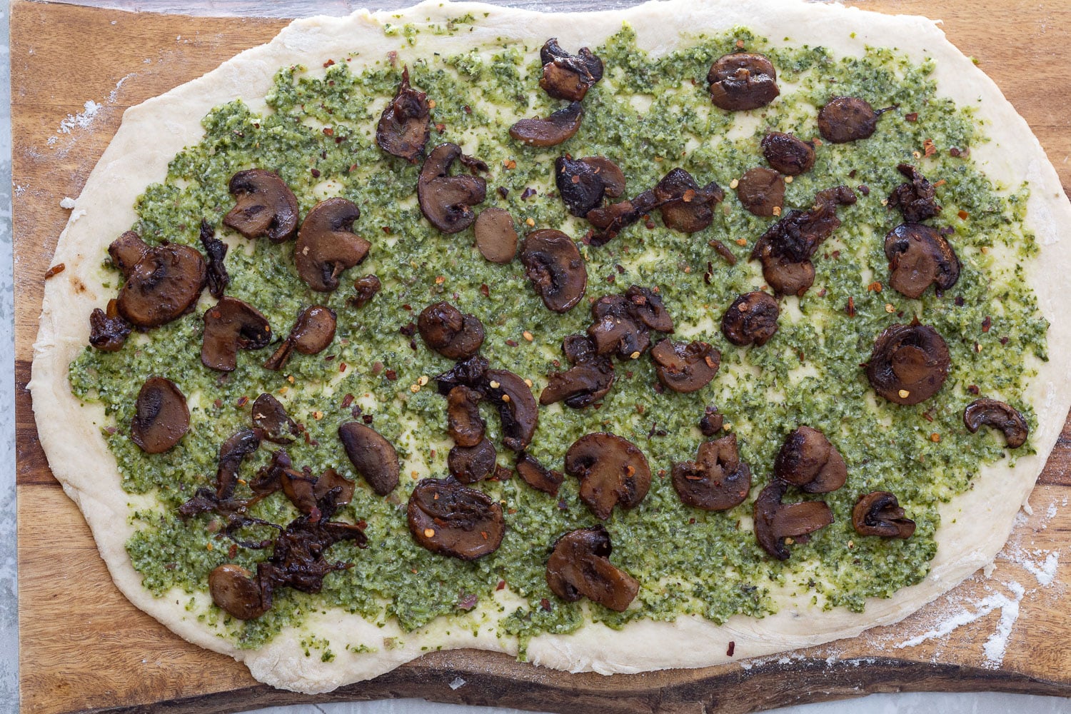 pizza rolls recipe sauteed mushrooms being sprinkled onto rolled out pizza dough spread with pesto