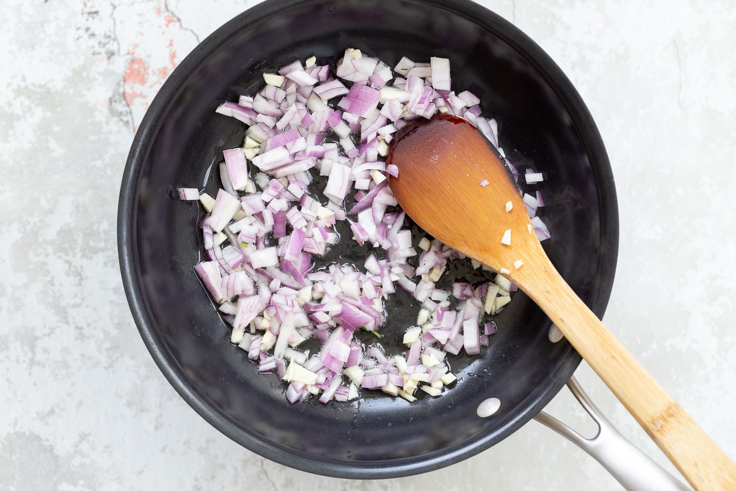 spinach pasta recipe chopped red onions being sauteed in a black skillet