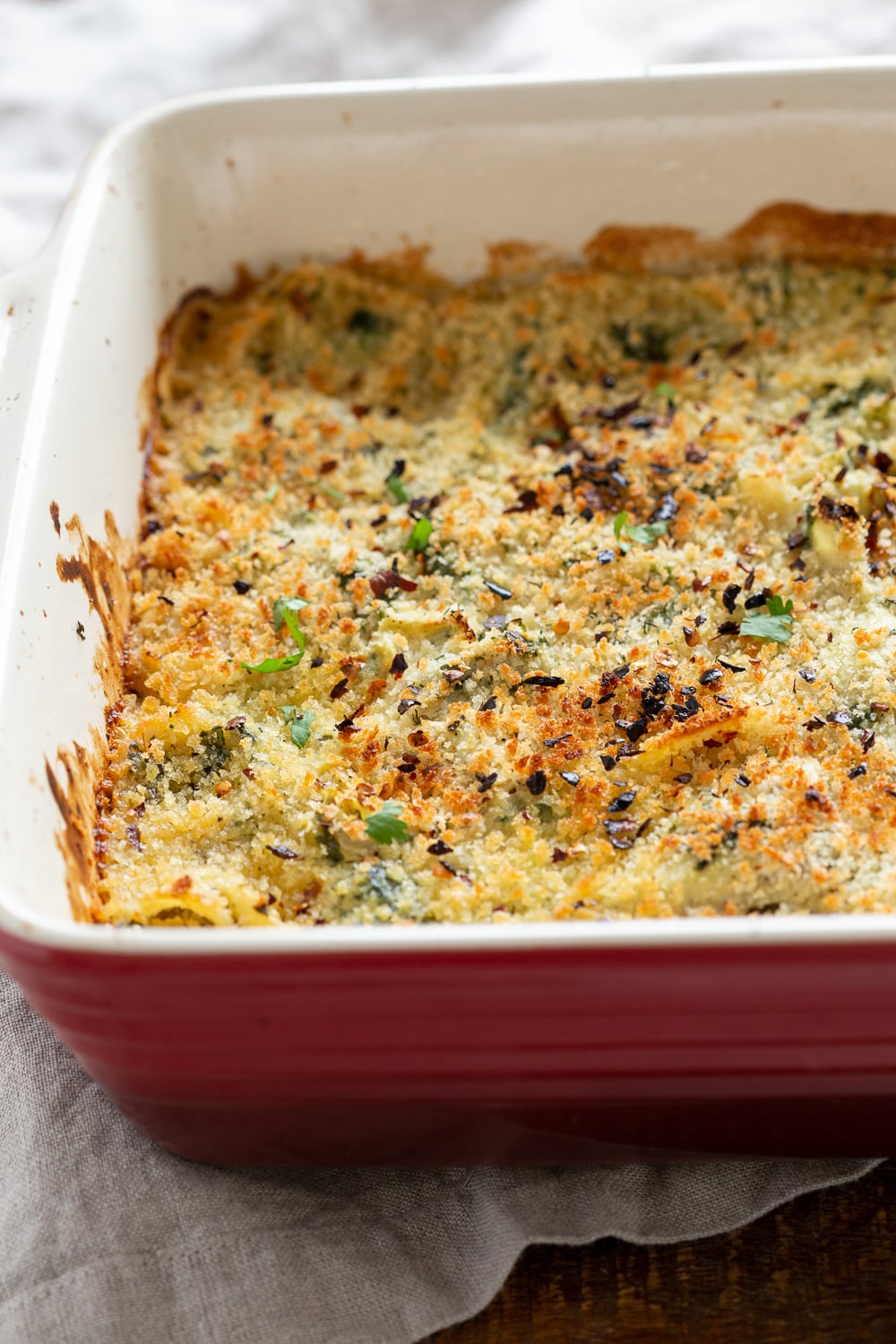 spinach pasta recipe side view close up of a red casserole dish with creamy vegan artichoke spinach pasta bake
