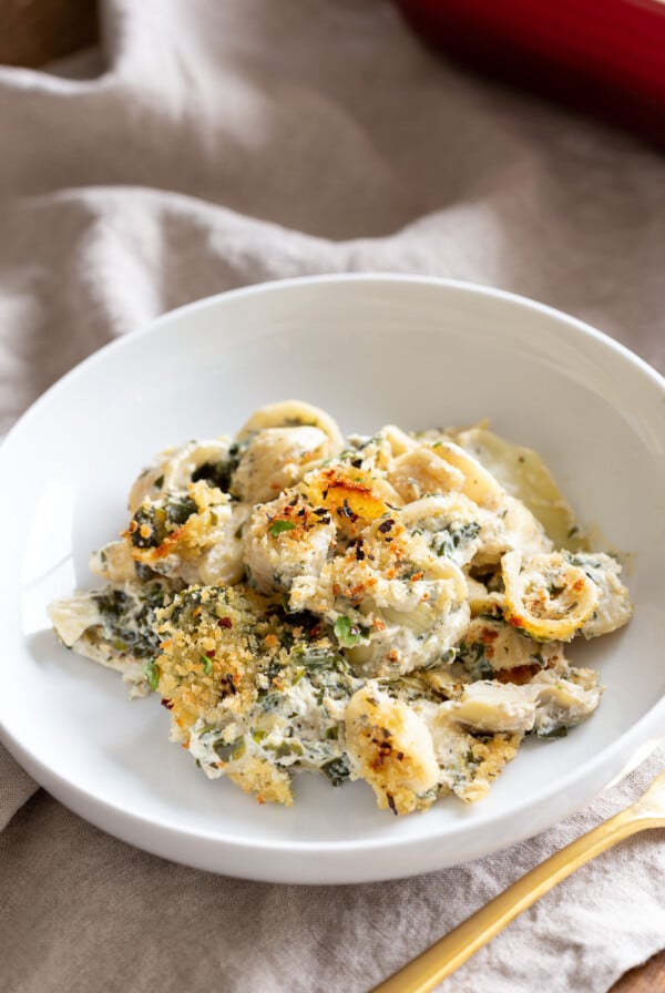 a serving of vegan spinach and artichoke pasta bake on a white plate
