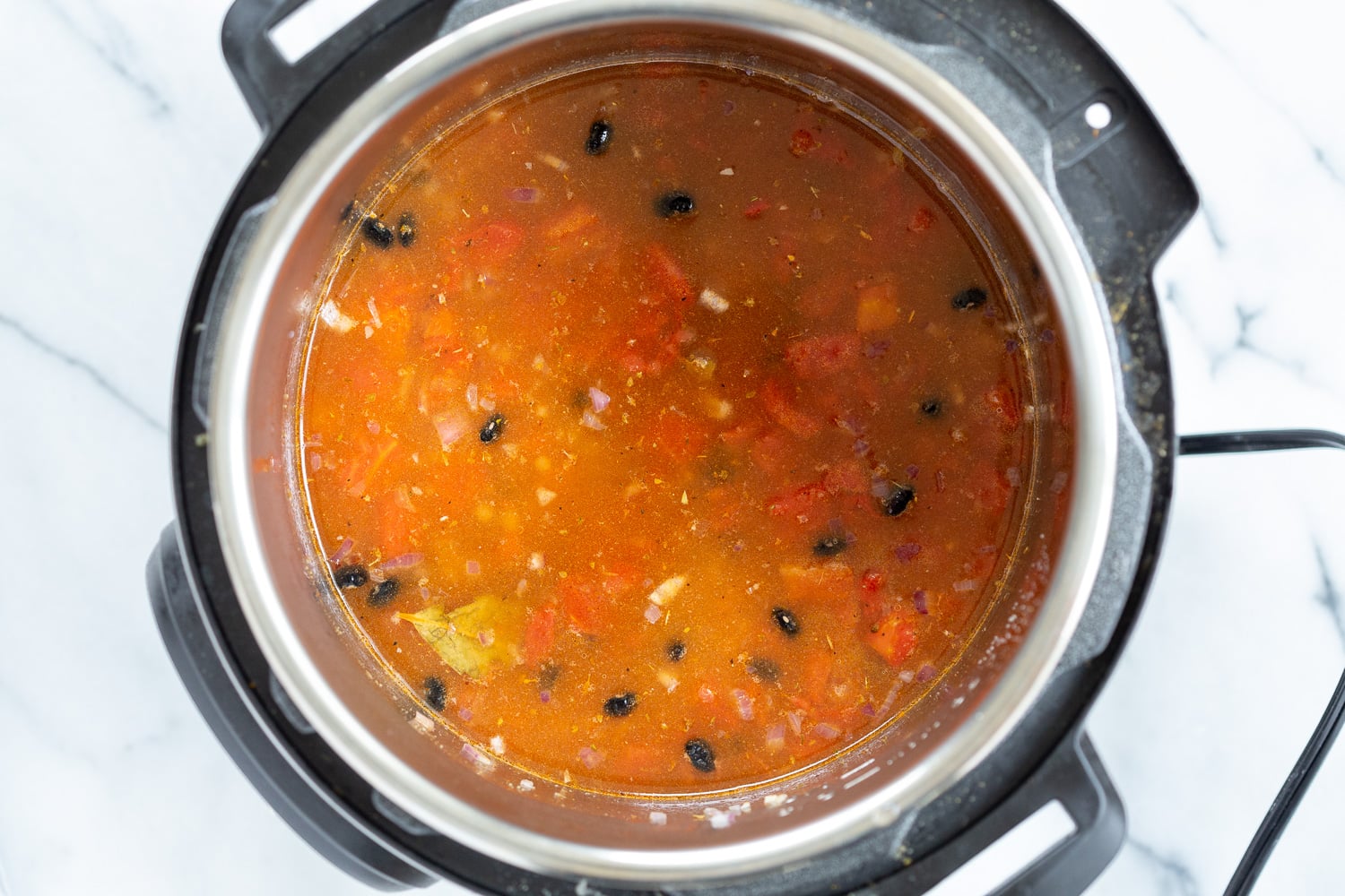 vegan black bean soup dried soaked beans being added to an Instant Pot filled with seasoned tomato broth
