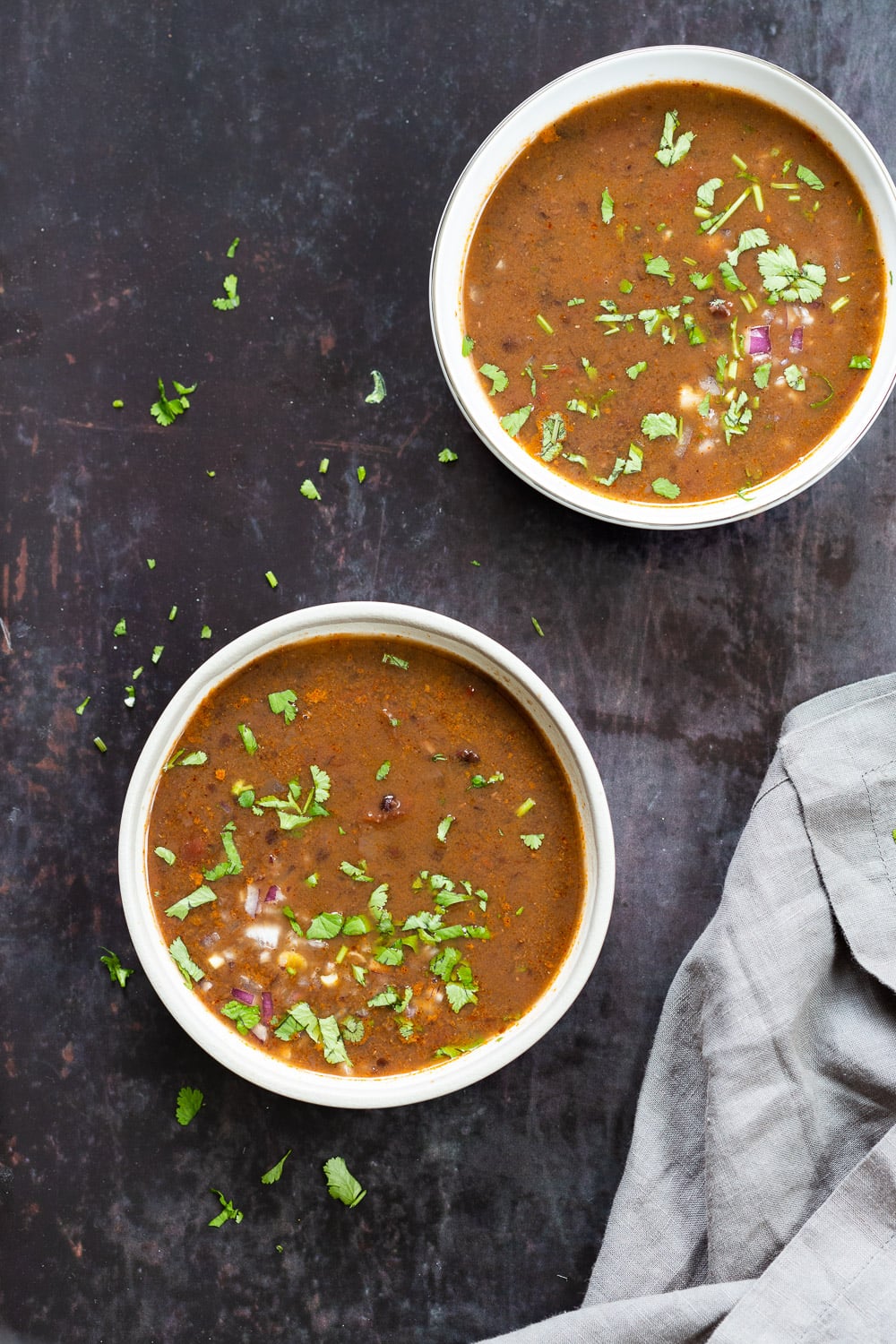 overhead shot of two bowls of vegan black beans soup sprinkled with chopped herbs 