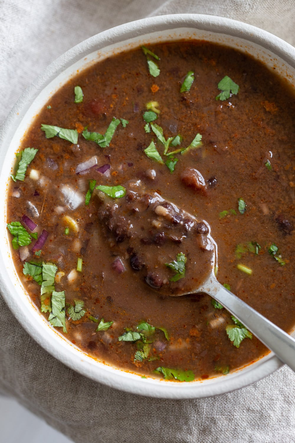 vegan black bean soup overhead shot of a white bowl with vegan black bean soup with a spoon dipping into the bowl