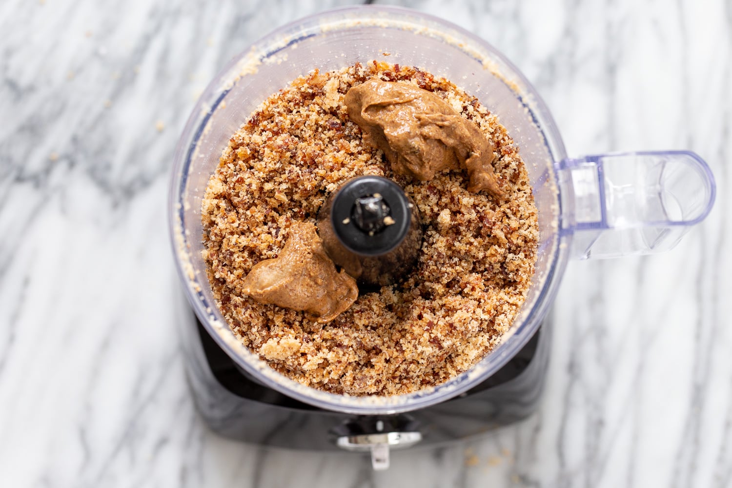 coconut balls almond butter being added to date and coconut mixture in a food processor to make energy balls