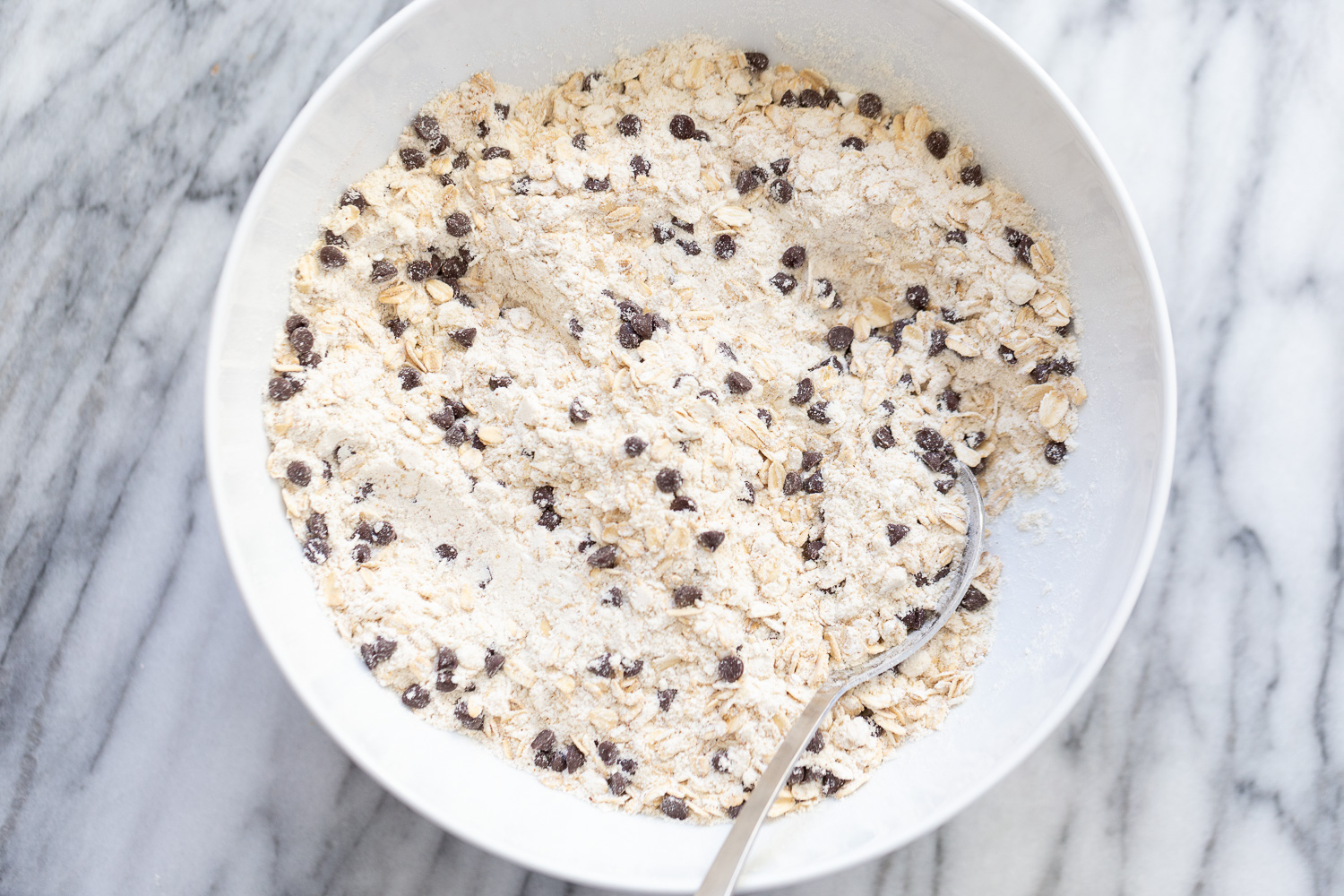 chocolate chip waffles dry ingredients for vegan oatmeal chocolate chip waffles being stirred in a white bowl