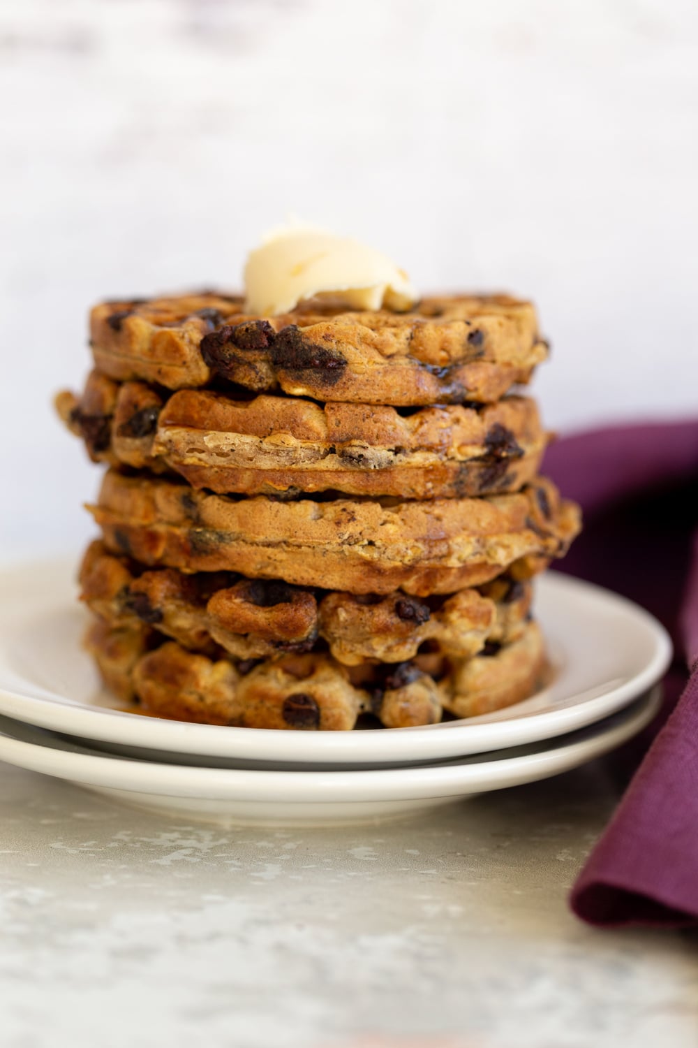 side view of a stack of vegan oatmeal chocolate chip waffles topped with vegan butter