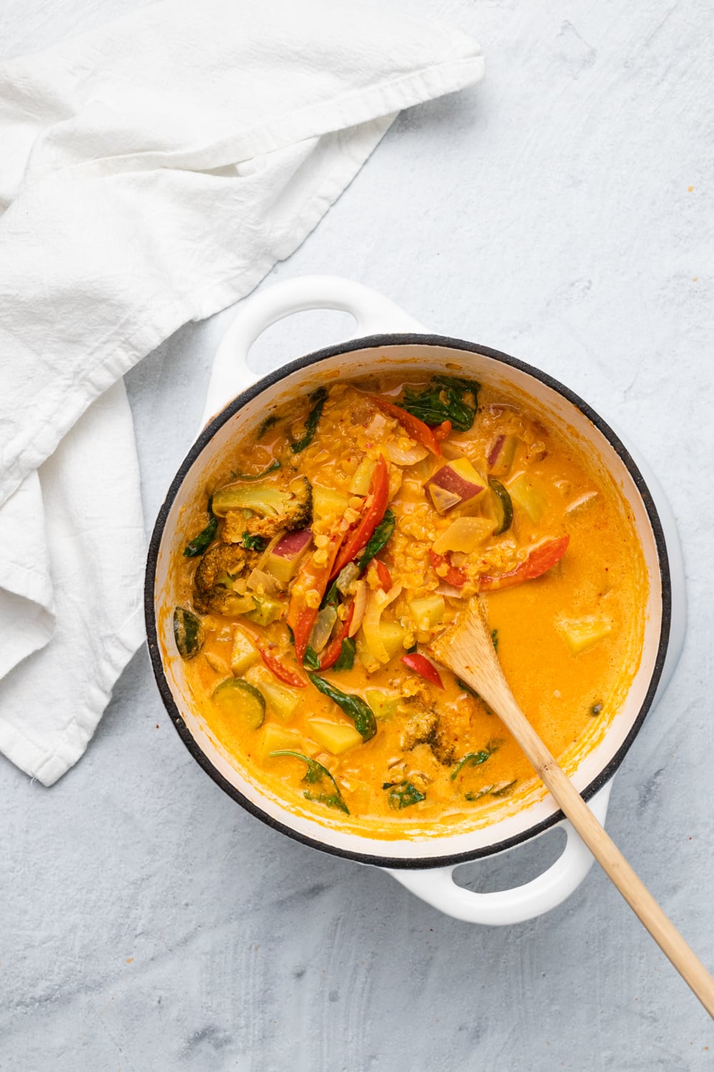 overhead shot of a white ceramic pot filled with vegan red lentil sweet potato curry 