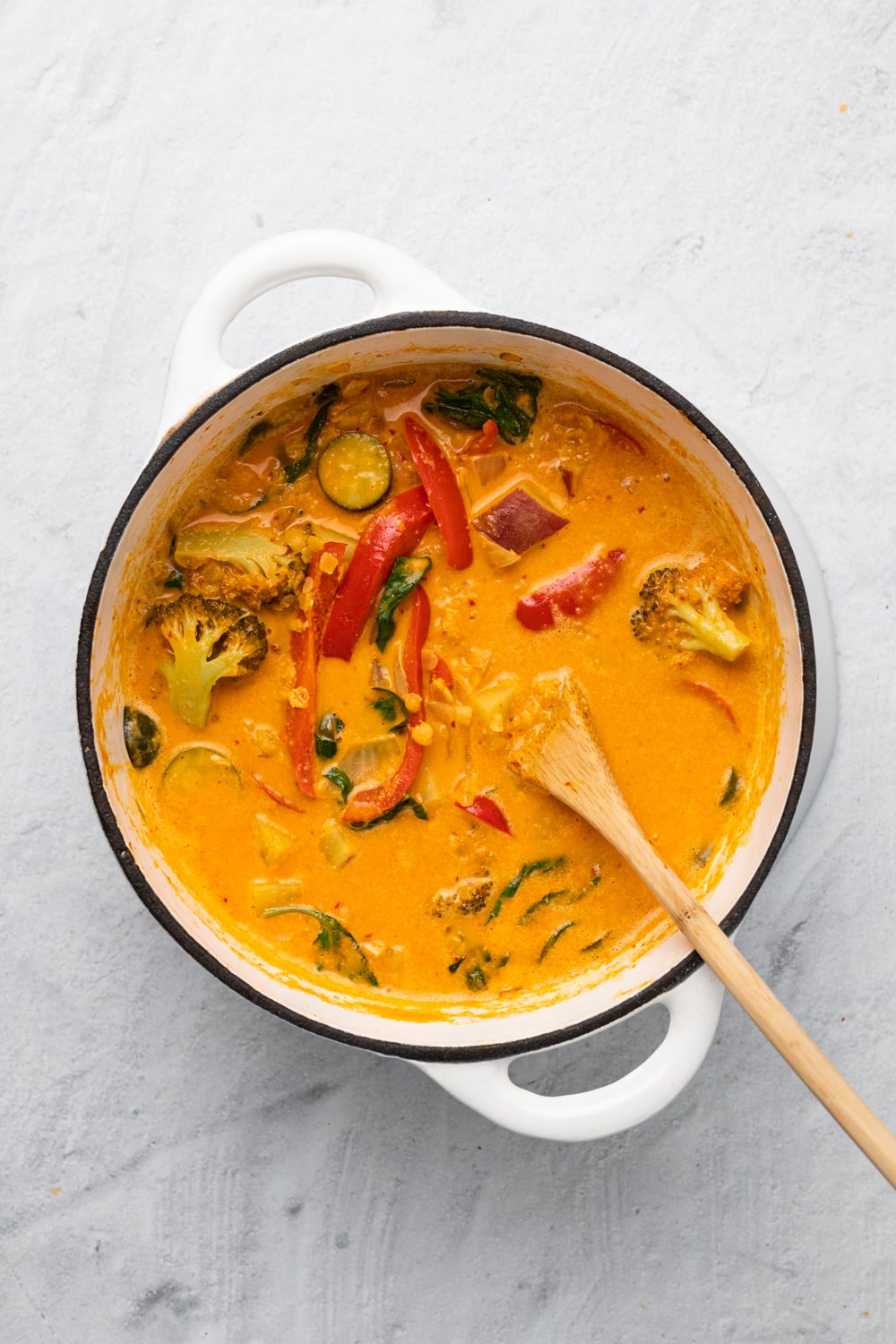 overhead shot of a pot of vegan red lentil sweet potato curry in a white pot with a wooden spoon 