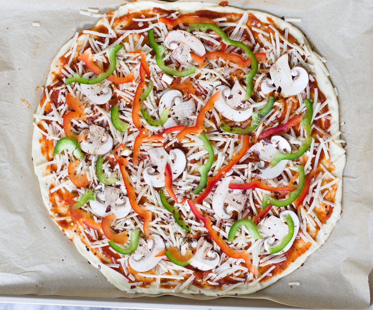 no yeast pizza dough overhead shot of unbaked vegan pizza on a baking sheet topped with vegetables and vegan cheese shreds