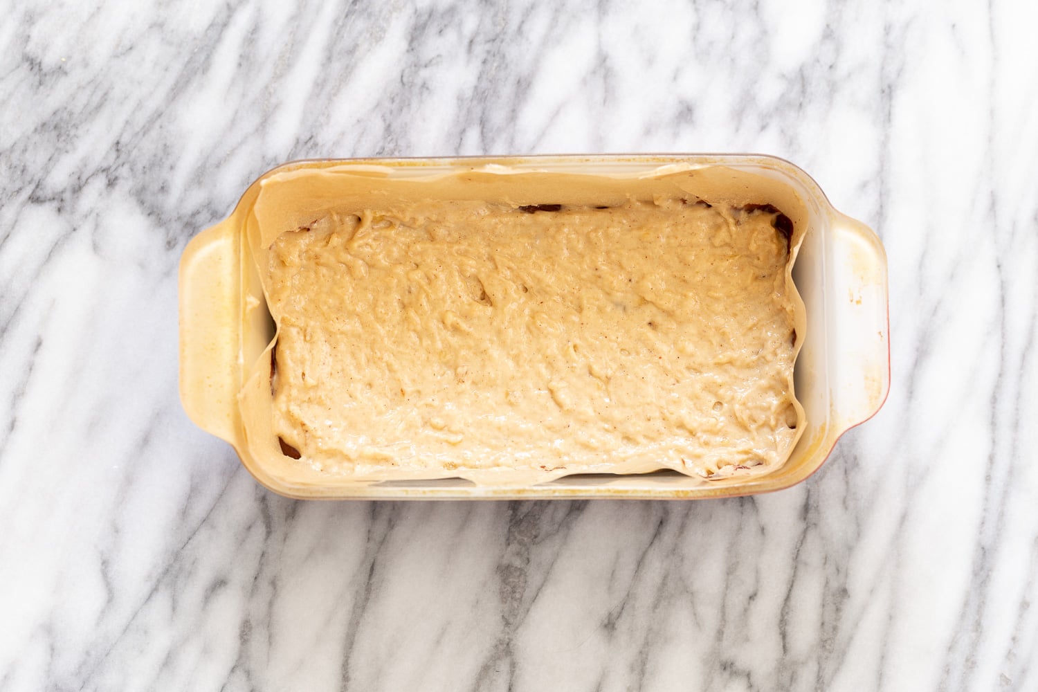 chocolate banana bread vanilla banana bread batter being scooped on top of dark batter to make marbled loaf