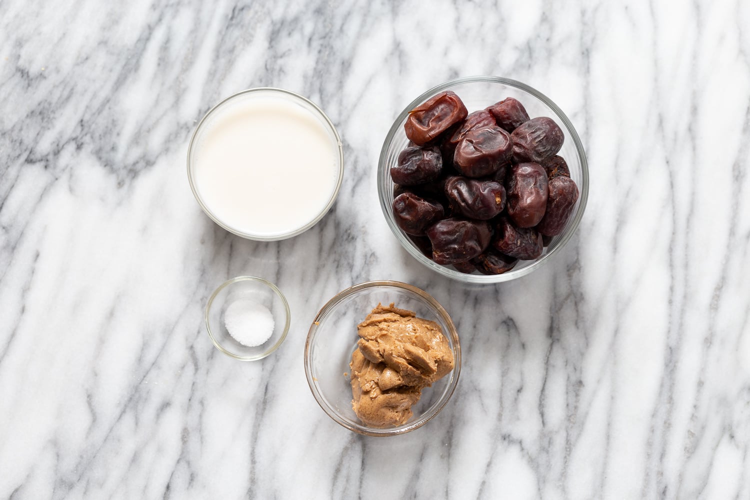 snickers recipe small glass dishes with plant based milk, dates, nut butter and salt on a kitchen counter
