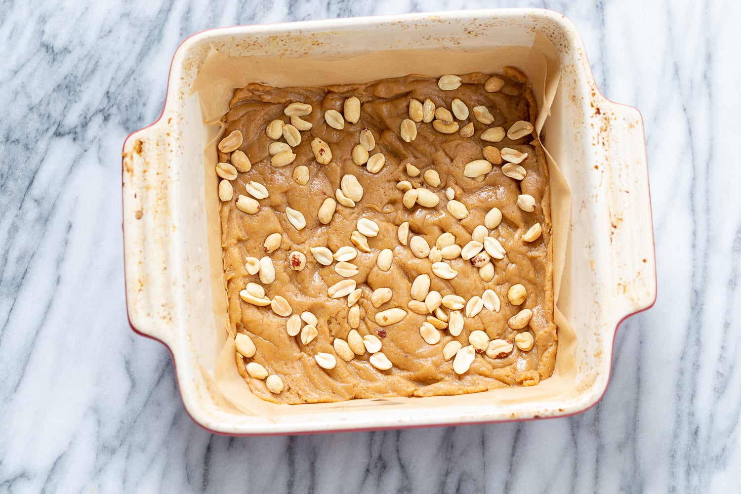 snickers bars recipe peanuts being sprinkled on cookie base to make vegan snack bars