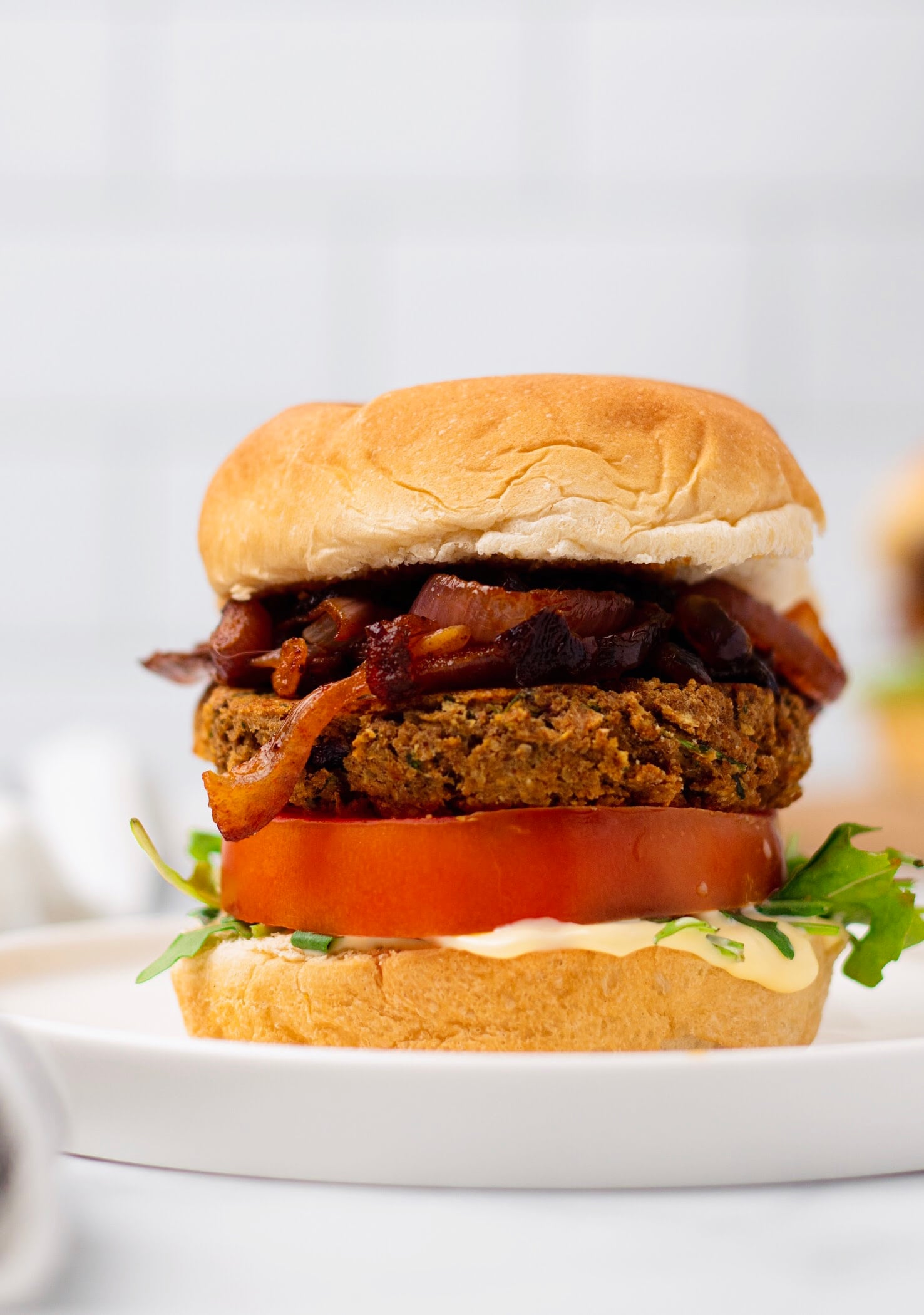 chickpea burger side view of a vegan chickpea burger with caramelized onion, tomatoes, hummus and lettuce
